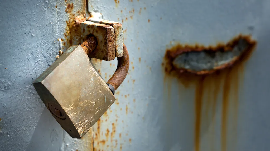 A rusty padlock on a hasp on a rust-speckled metal door. 